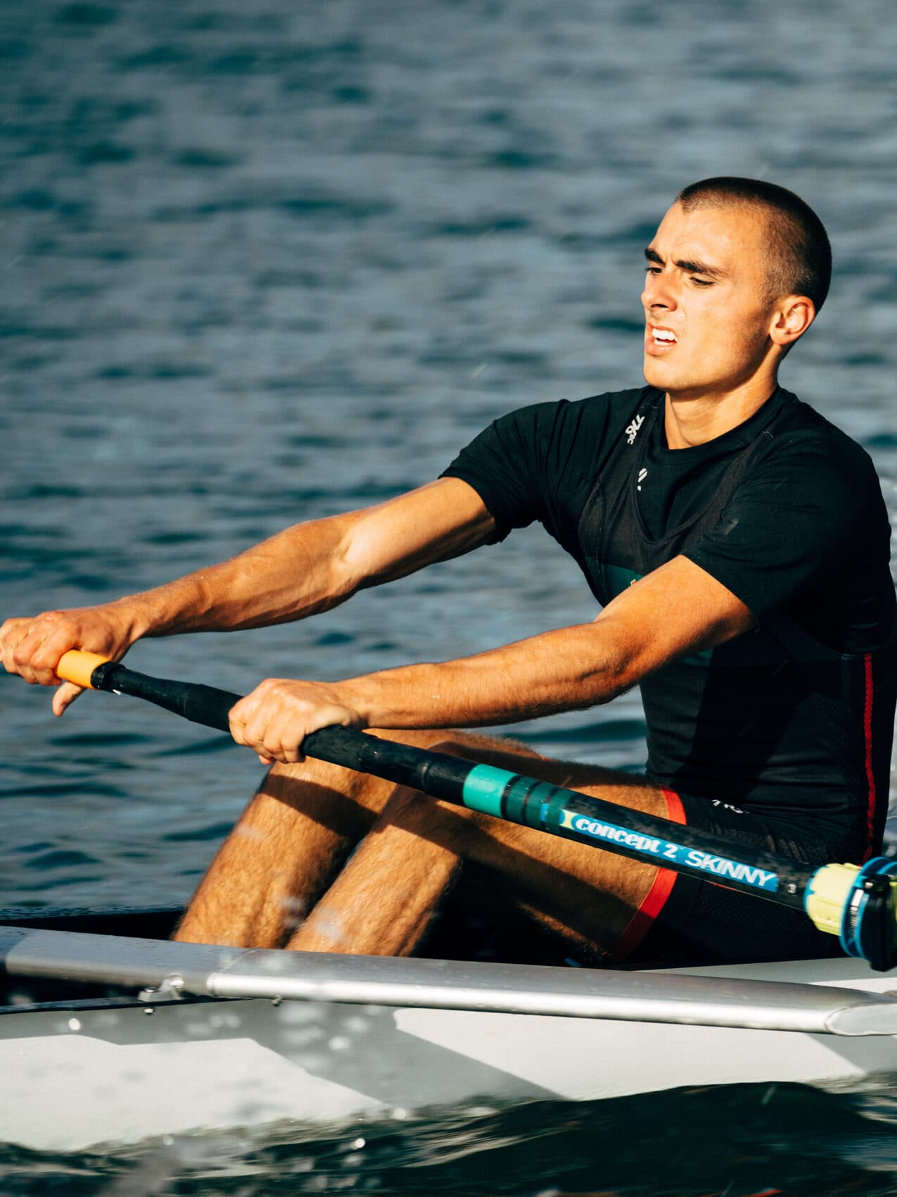 A men's rower pulls through the stroke in late afternoon sun on the Estuary